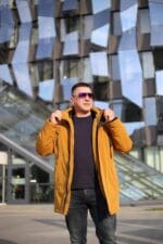 Расстегнутая зимняя куртка горчичного цвета, вид спереди на модели.
