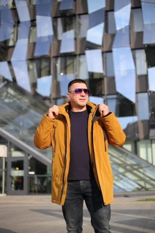 Розстібнута зимова куртка гірчичного кольору, вид спереду на моделі.